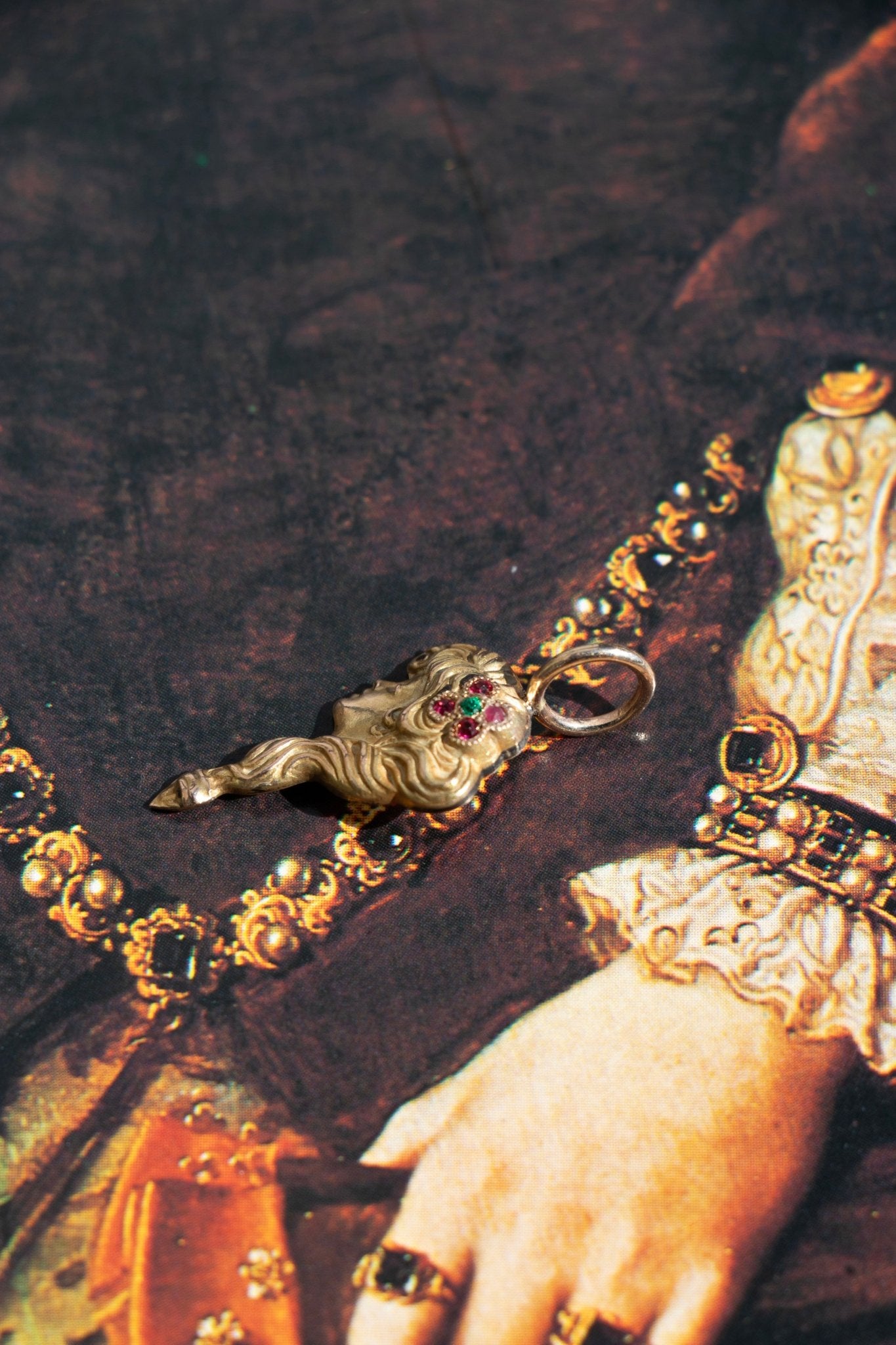 the side view of a 14k antique art nouveau lady charm photographed on a book - queer and trans fine jewelry by lettuce goods / 14karatdoll