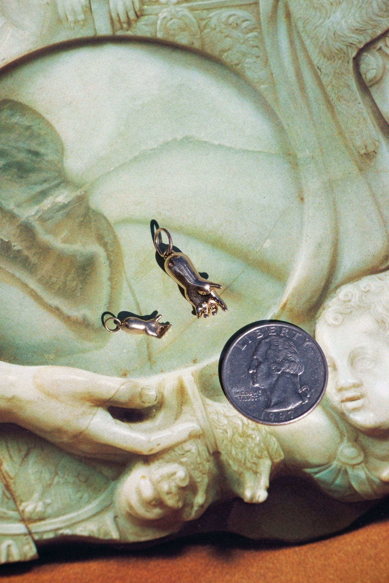 small and large 14k gold baby hand charms on a background for size comparison to a quarter – queer and trans fine jewelry by lettuce goods / 14karatdoll